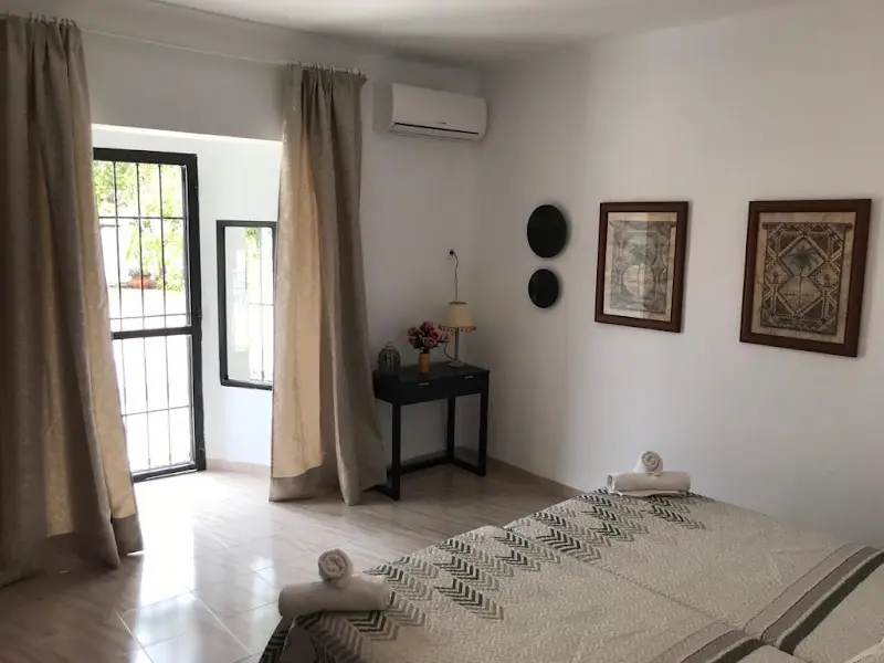 Dormitorio con cama de colcha estampada, toallas enrolladas y puerta con reja al patio