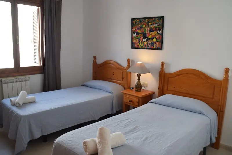 Dormitorio con dos camas individuales de madera, colchas azules y un cuadro colorido