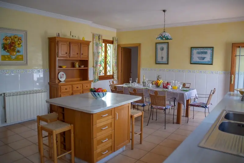 Cocina amplia con isla, aparador de madera y mesa de comedor puesta junto a la ventana