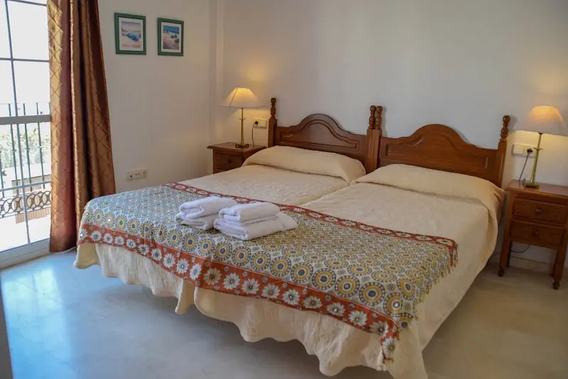 Dormitorio con dos camas individuales de madera, colcha estampada y toallas preparadas