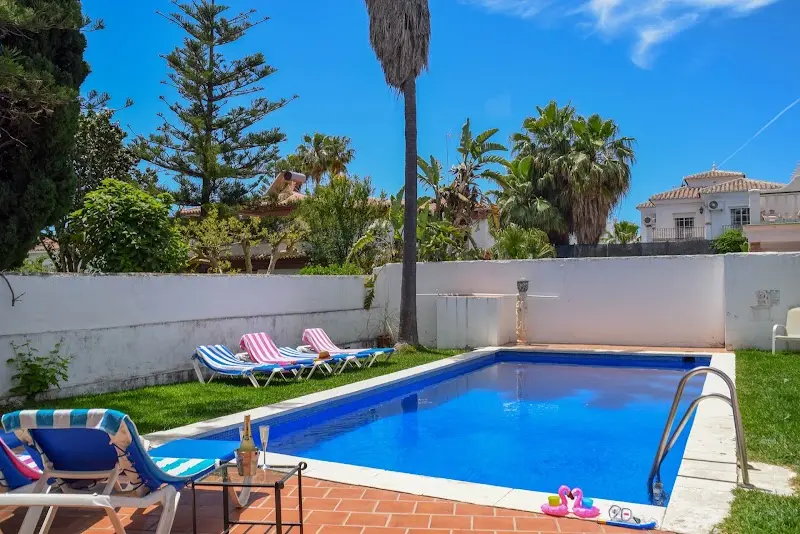 Piscina privada rodeada de césped, tumbonas de rayas y palmeras junto al muro blanco