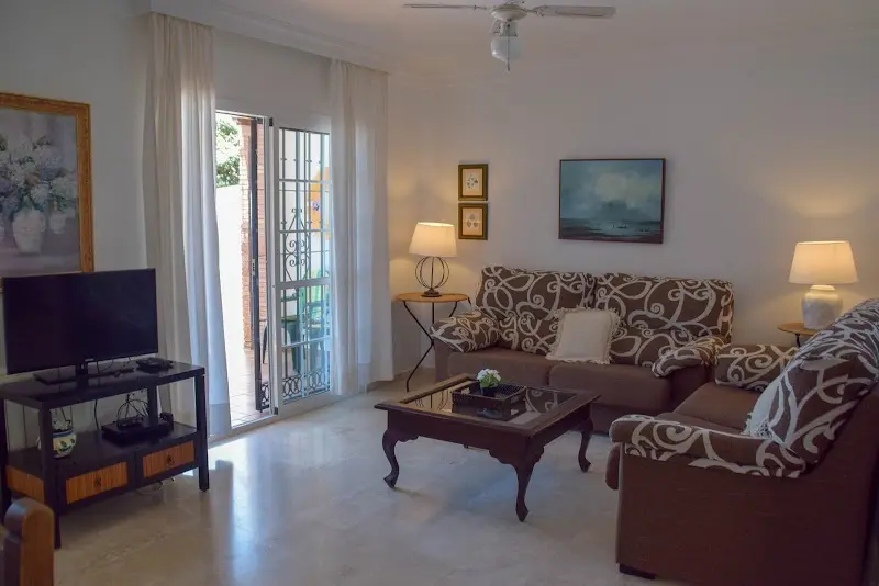 Salón con sofás estampados, mesa de centro, televisor y puerta al exterior