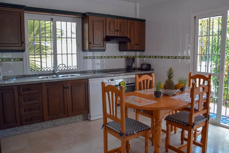 Cocina con muebles de madera oscura, lavavajillas y mesa de comedor con cuatro sillas
