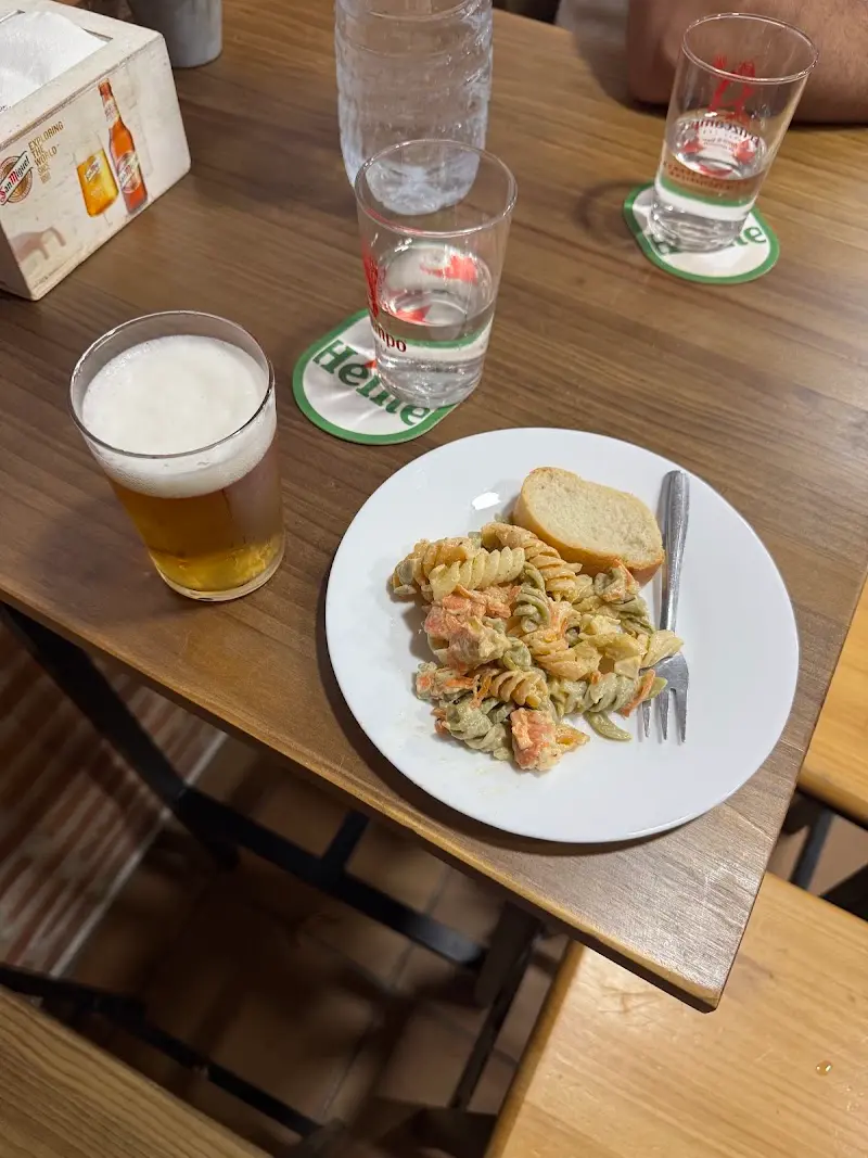Tapa de ensalada de pasta con pan y una caña de cerveza en una mesa de madera