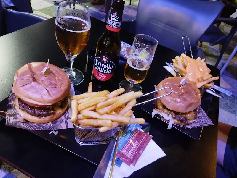 Dos hamburguesas con patatas fritas en cestita, una con salsa de queso, y cervezas