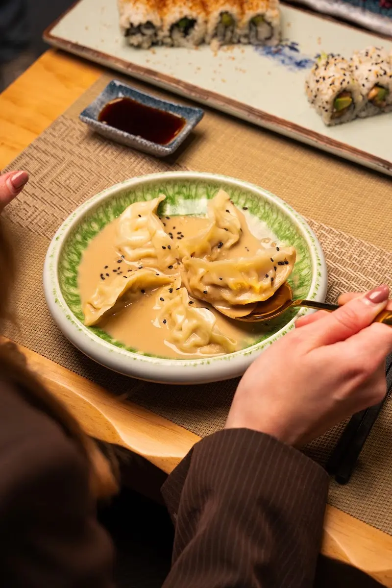 Gyozas en salsa con sésamo negro y, al fondo, una bandeja de uramakis