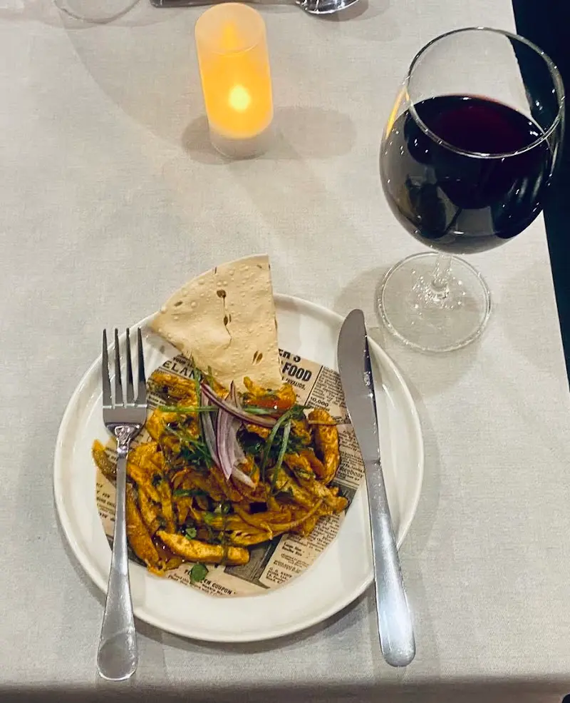 Plato de tiras de pollo especiado con cebolla roja y papadum, con una copa de vino tinto