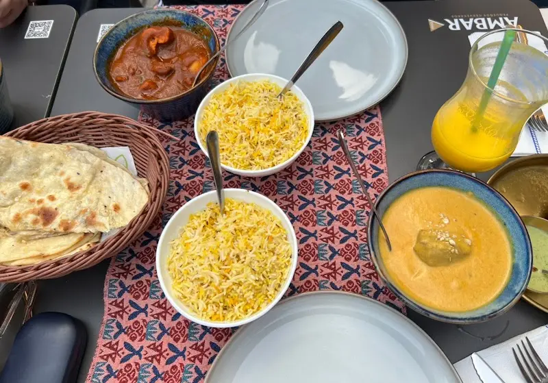Mesa con arroz amarillo, currys en cuencos, pan naan y un zumo de naranja