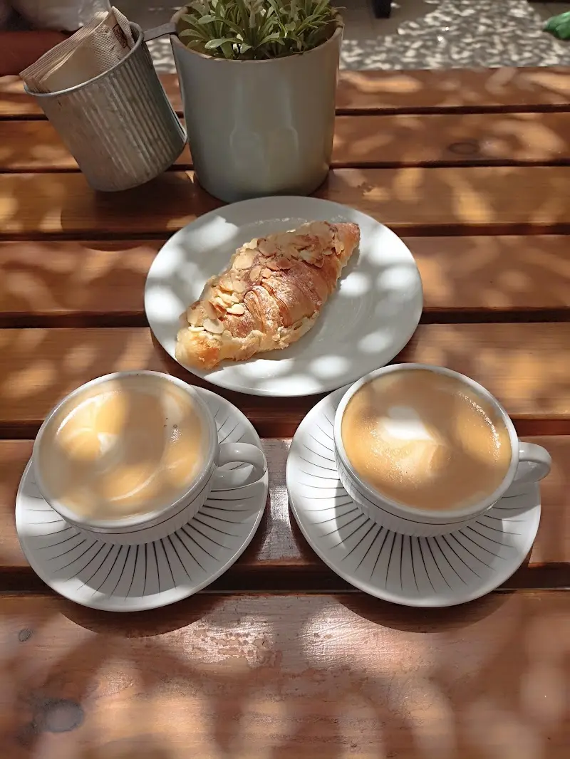 Cruasán de almendras y dos cafés con leche en una mesa de madera al sol