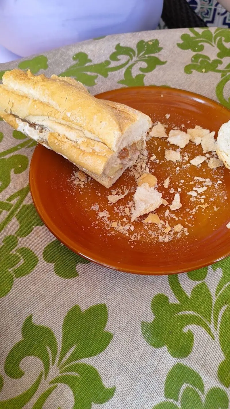 Bocadillo en barra de pan crujiente sobre un plato de barro con migas