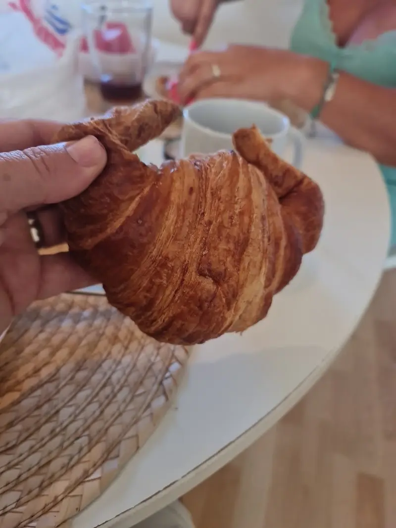 Croissant grande de hojaldre tostado sostenido en la mano junto a una taza de café