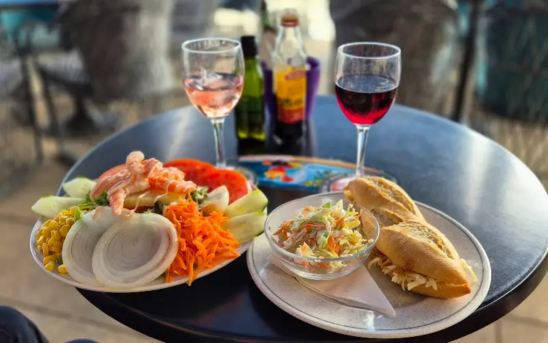 Ensalada con gambas, zanahoria y maíz, bocadillo con ensalada de col y copas de vino