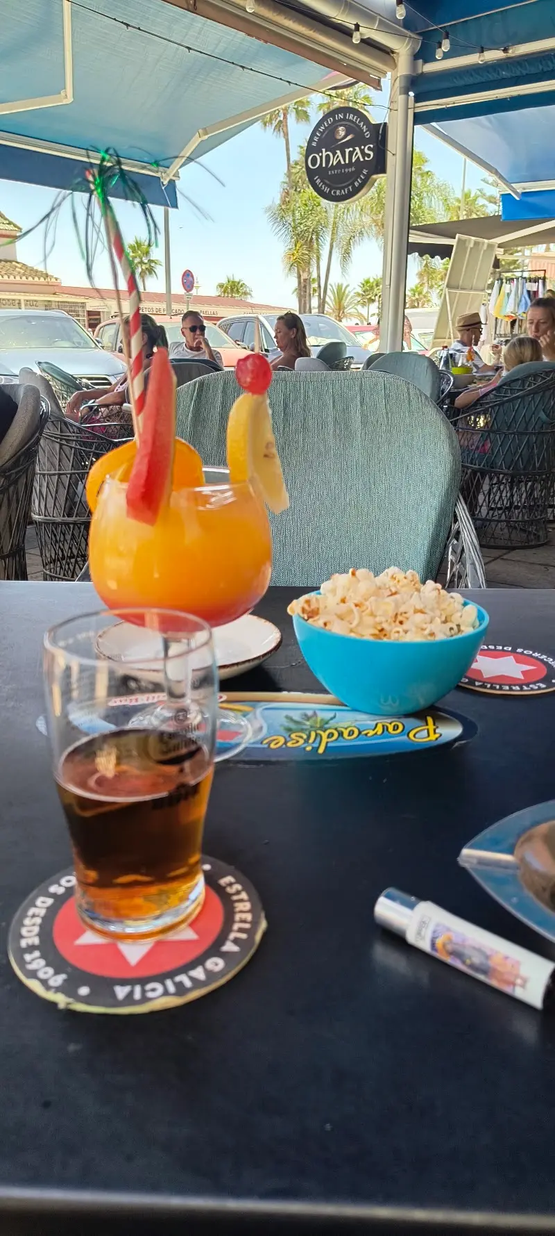 Cóctel naranja decorado con fruta, cerveza y cuenco de palomitas en la terraza
