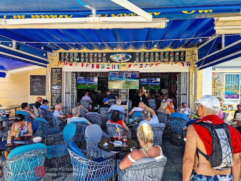 Terraza llena de clientes con sillones azules y partido de tenis en las pantallas