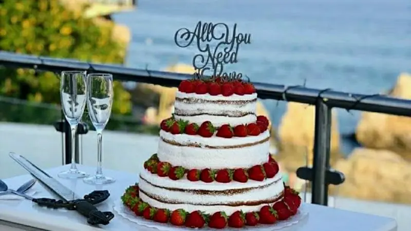 Tarta nupcial de tres pisos con fresas y copas de cava en una terraza frente al mar