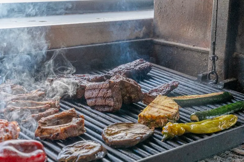 Carnes y verduras humeando en la parrilla argentina: costillas, entrecot, calabacín y pimientos