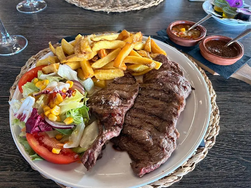 Entrecot a la parrilla con patatas fritas, ensalada y cuencos de chimichurri
