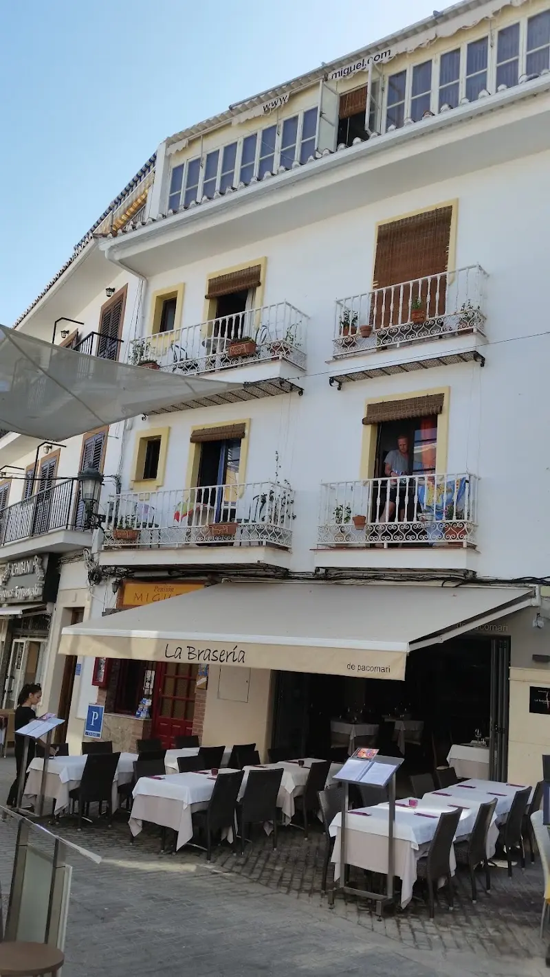 Fachada blanca de la Pensión Miguel con balcones de forja sobre la terraza de La Brasería