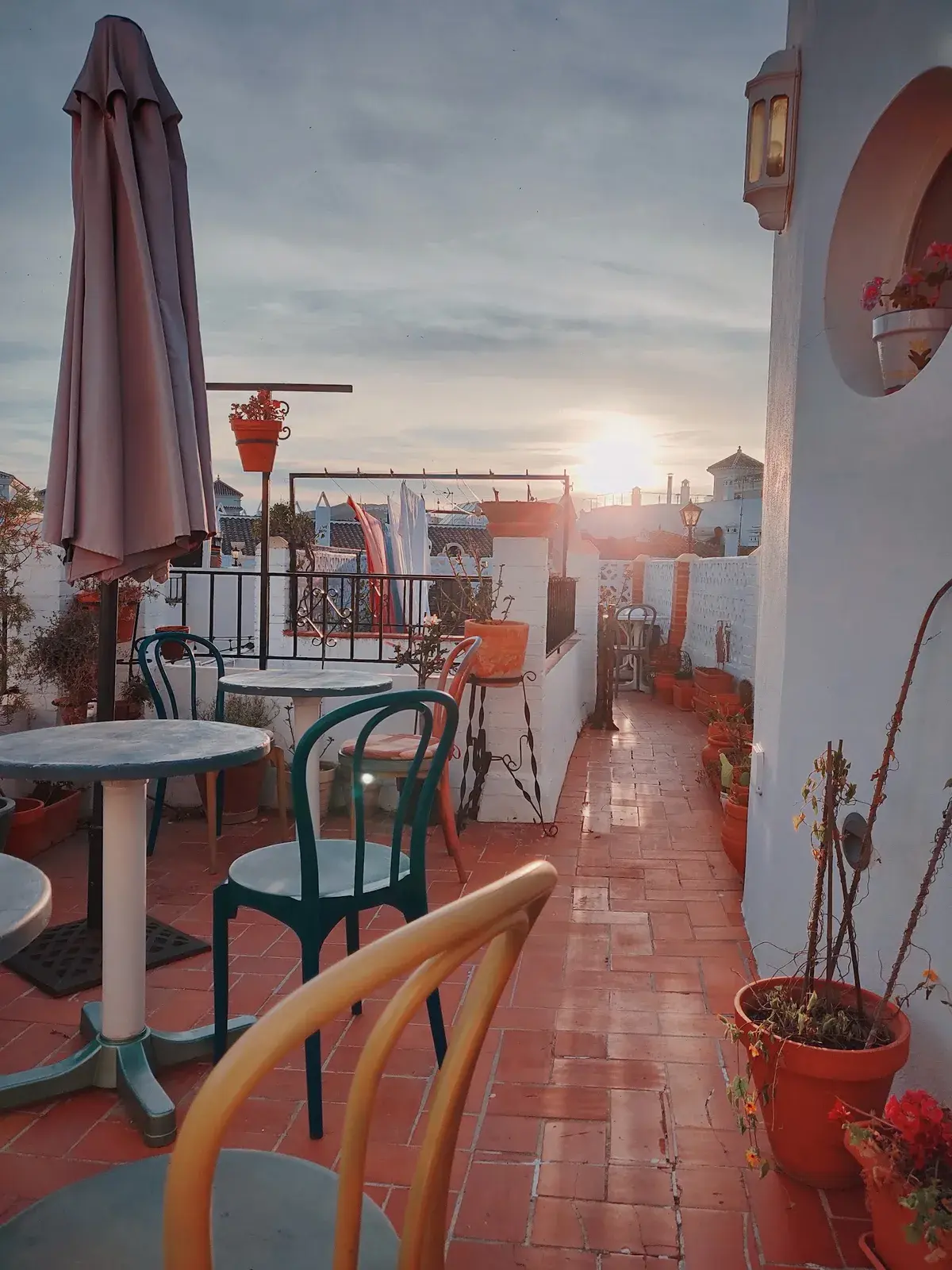 Terraza de la Pensión Miguel con mesas, macetas y el sol poniéndose sobre los tejados