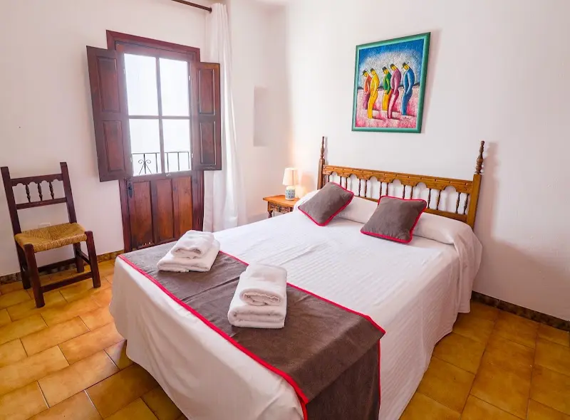 Habitación de la Pensión Sevillano con cama de matrimonio, cabecero de madera y ventana con contraventanas