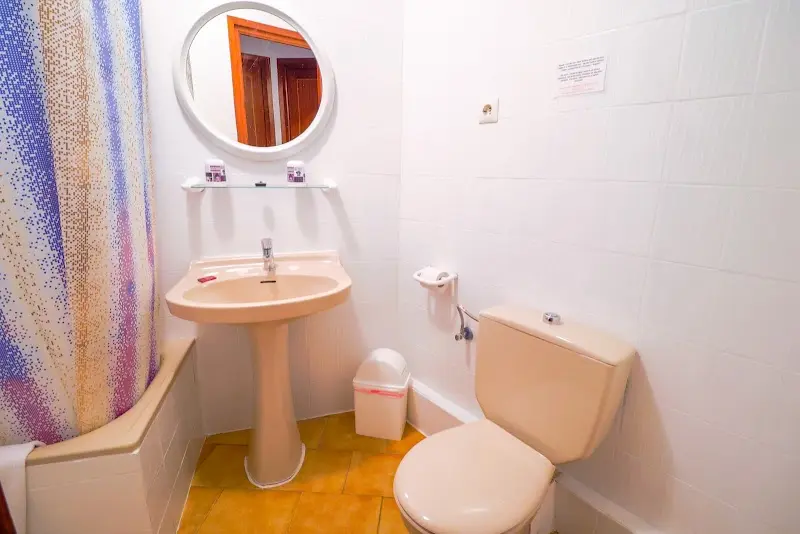 Baño con bañera y cortina de colores, lavabo de pie y espejo redondo