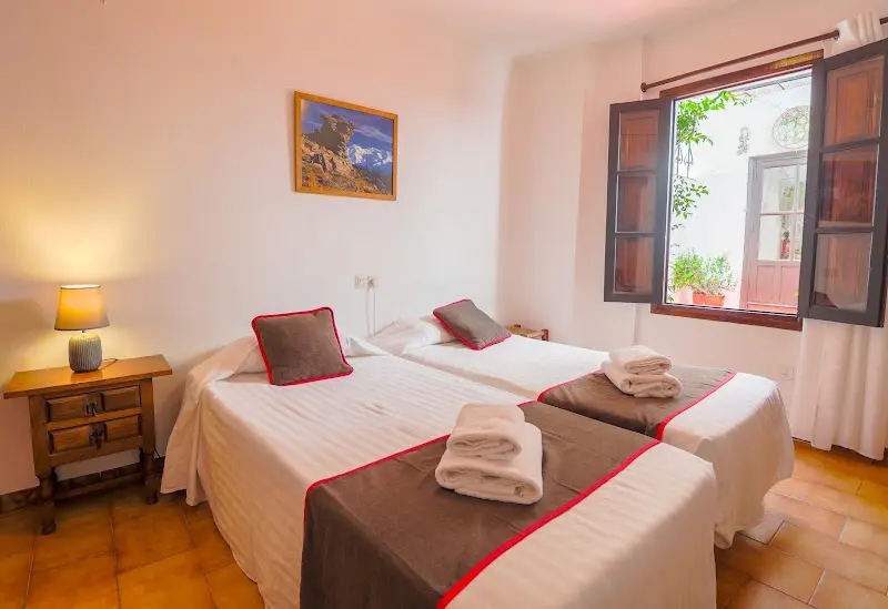 Habitación con dos camas, toallas dobladas y ventana abierta a un patio con macetas