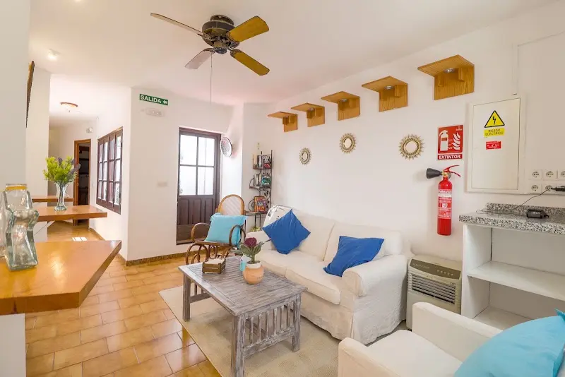 Sala común con sofá blanco de cojines azules, mesa baja y ventilador de techo