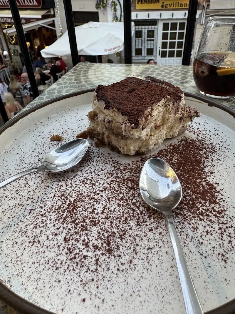 Ración de tiramisú espolvoreado con cacao, con la calle animada al fondo