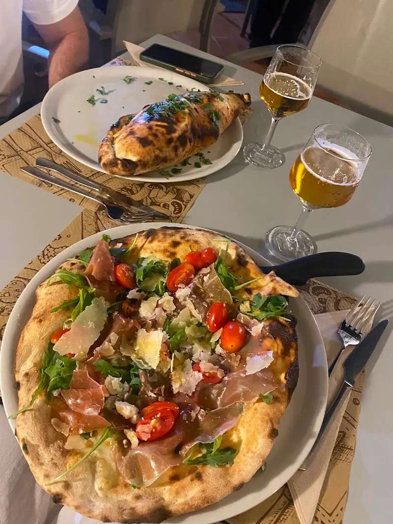 Pizza con jamón curado, rúcula, tomates cherry y lascas de queso, junto a un calzone