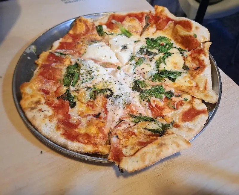 Pizza de masa fina con tomate, mozzarella y hojas verdes en bandeja metálica