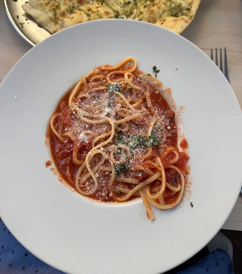 Espaguetis con salsa de tomate y queso rallado, con pan de ajo al fondo