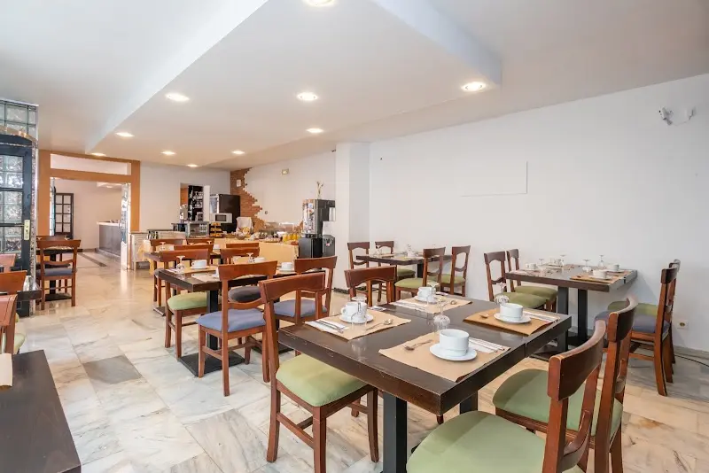 Comedor interior con mesas de madera, sillas verdes y servicio de desayuno al fondo