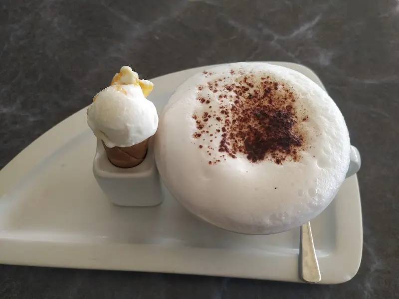 Capuchino con cacao espolvoreado y un pequeño cucurucho de helado en una bandeja blanca