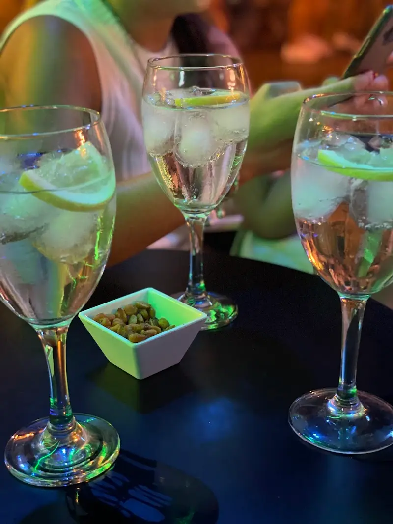 Tres copas de gin-tonic con limón y un cuenco de frutos secos bajo luz azul