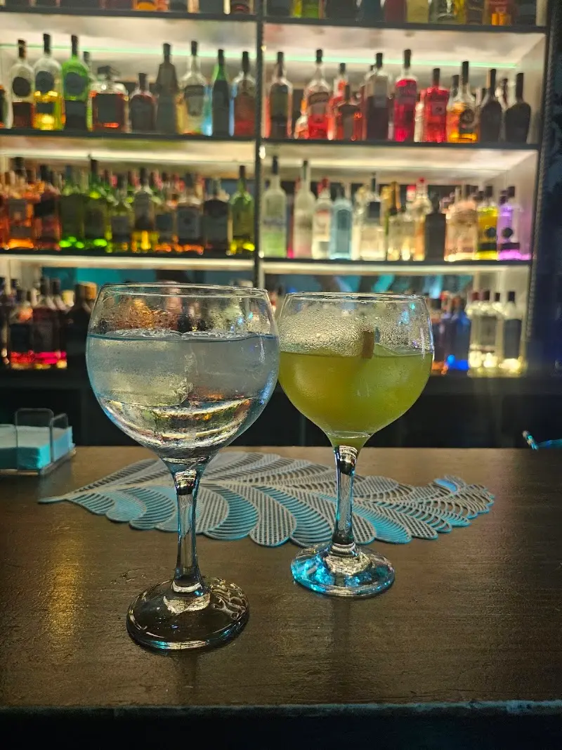 Dos copas de balón sobre la barra, una transparente y otra amarilla, ante estantes de botellas