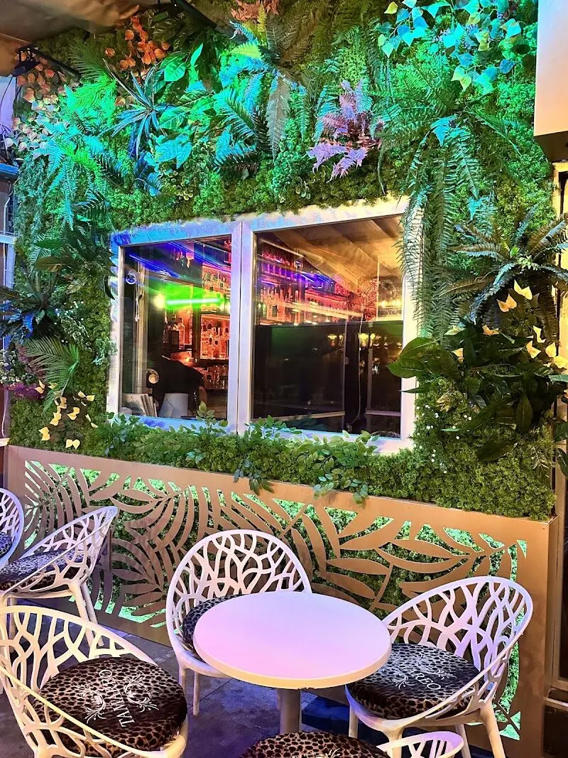Rincón de terraza con pared vegetal, ventana a la barra y sillas blancas caladas