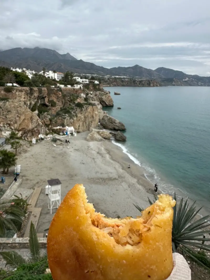 Empanada mordida con relleno de carne mechada sobre una playa de Nerja