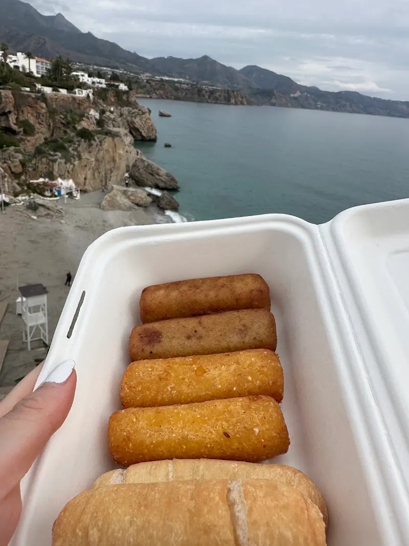 Caja con tequeños y pan frente a los acantilados y una playa con torre de socorrista