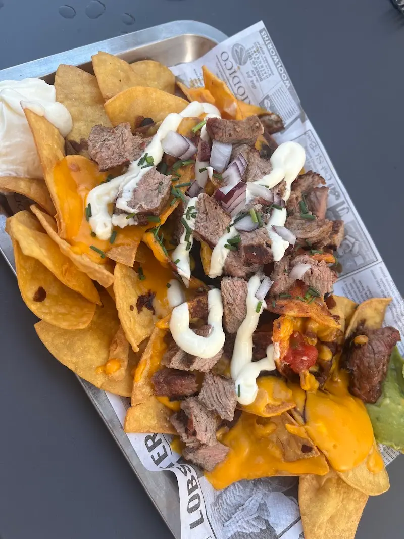 Nachos con trozos de carne, queso cheddar fundido, cebolla morada y salsa de nata agria