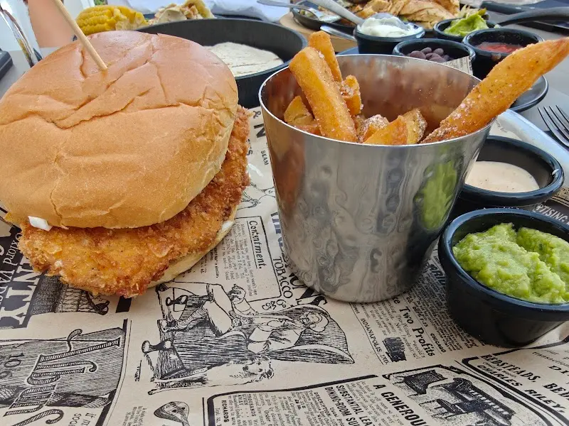 Hamburguesa de pollo crujiente con patatas fritas en vaso metálico y guacamole