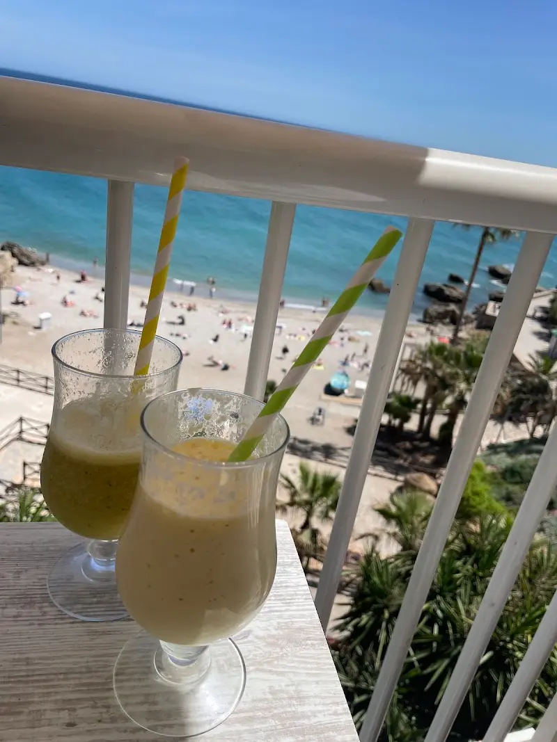 Dos batidos de fruta con pajitas en una barandilla con vistas a la playa y al mar