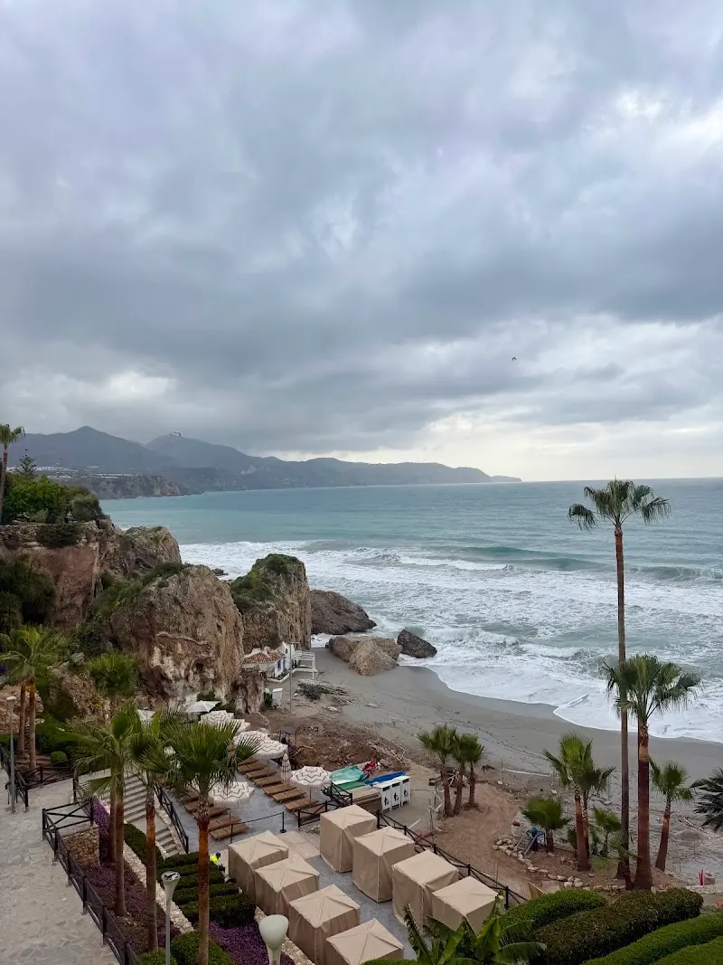 Vista de la playa bajo los acantilados con palmeras y cabañas, en un día nublado