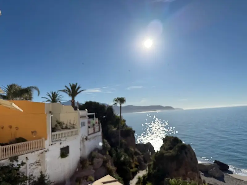 Costa de Nerja a contraluz con casas blancas, palmeras y el sol sobre el mar