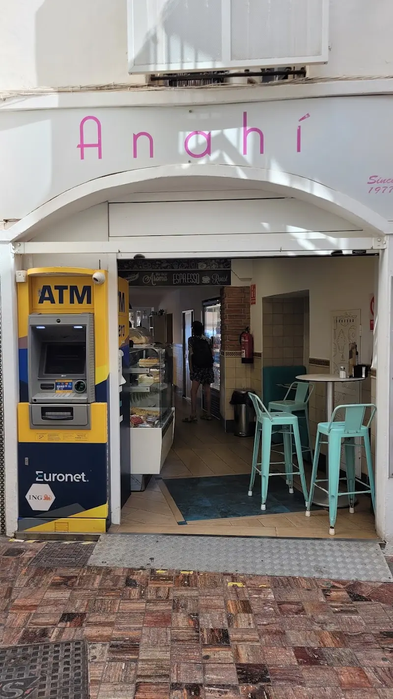 Entrada de la cafetería Anahí con mostrador de bollería y taburetes turquesa