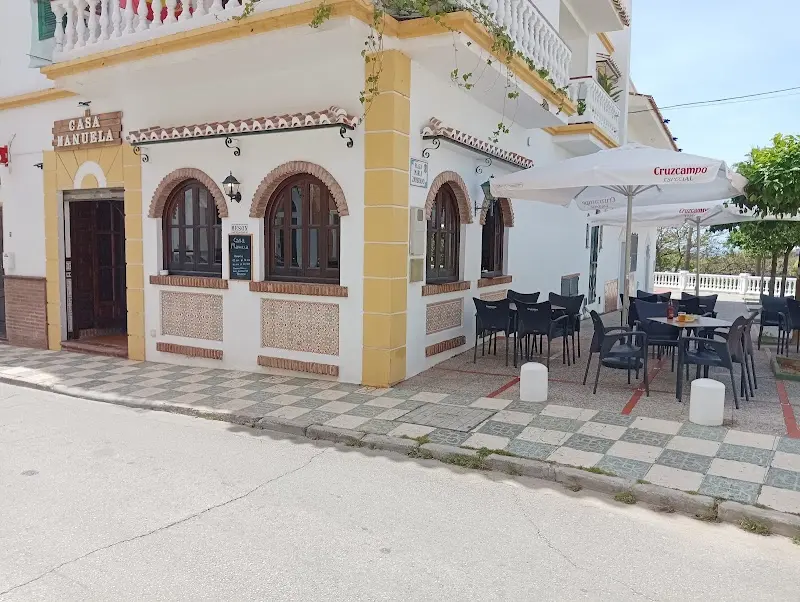 Fachada encalada de Casa Manuela con ventanas en arco, rótulo de madera y terraza con sombrillas