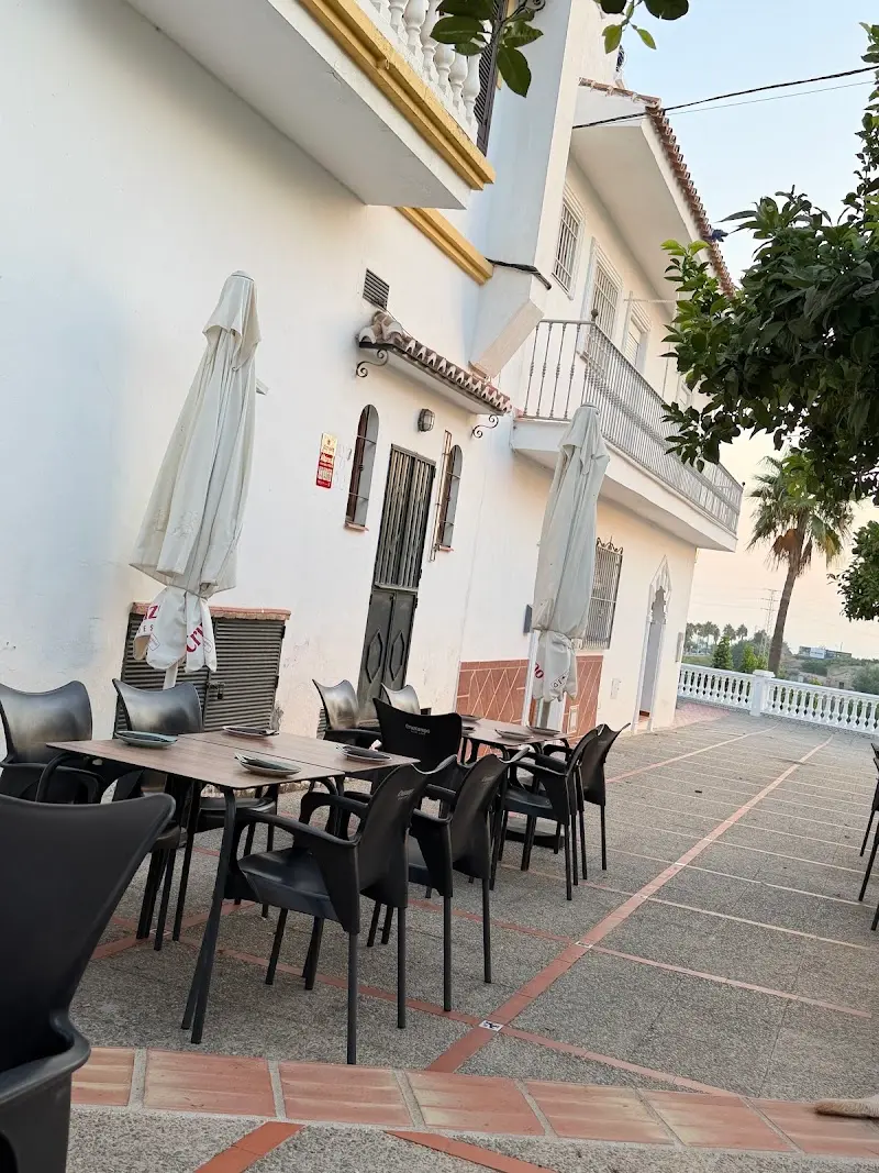 Mesas preparadas en la terraza junto a la fachada blanca, con sombrillas cerradas