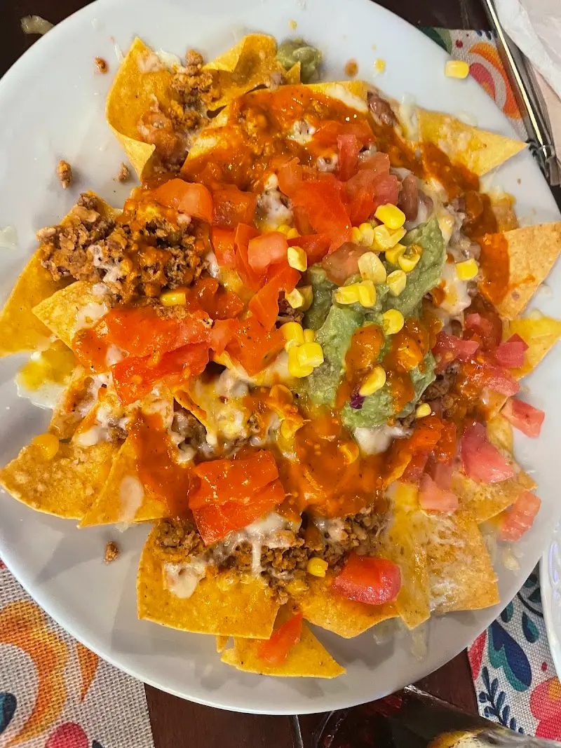 Nachos con carne picada, queso fundido, guacamole, tomate y maíz
