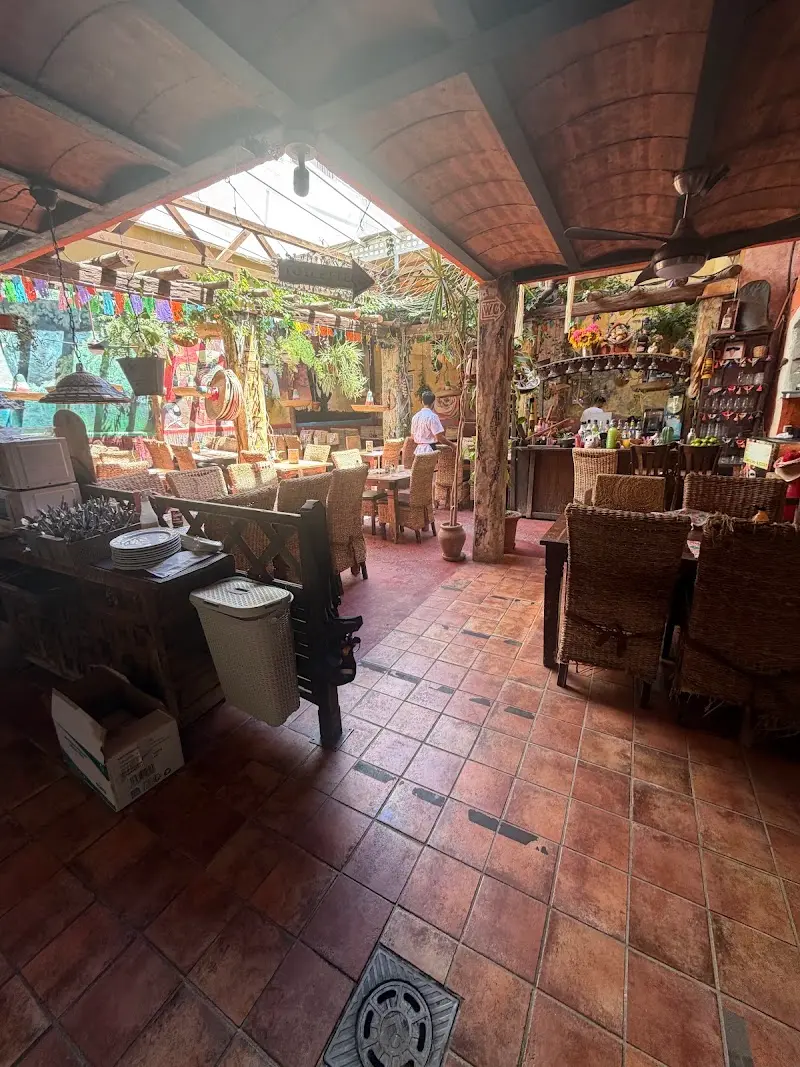 Patio interior con suelo de barro, sillas de mimbre, banderines de colores y techo acristalado