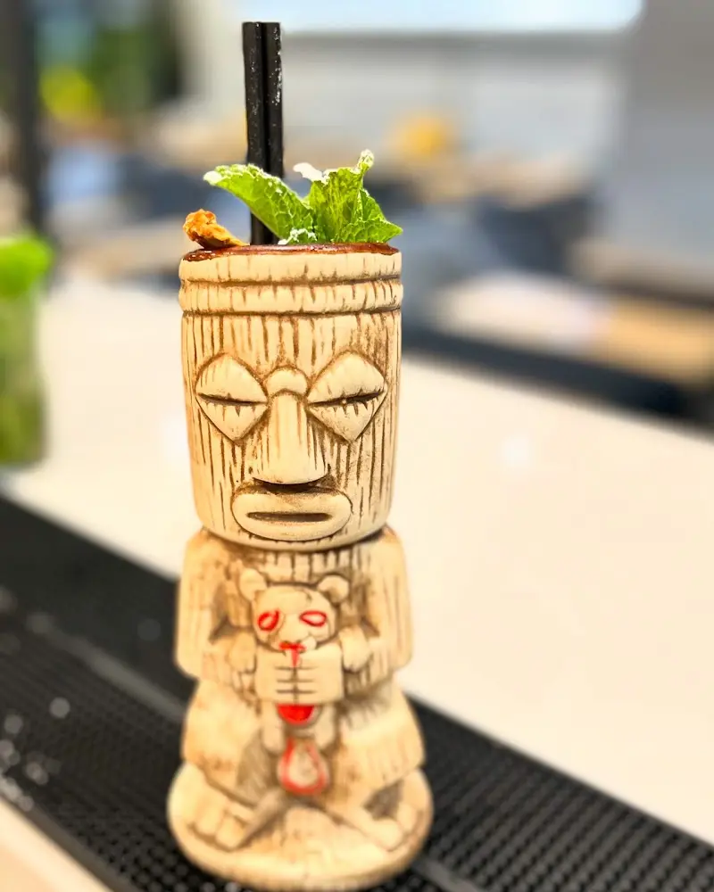 Cóctel servido en vaso tiki de cerámica con hojas de menta sobre la barra