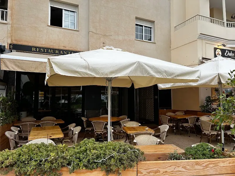 Terraza exterior con sombrillas blancas, mesas de madera y jardineras frente al restaurante